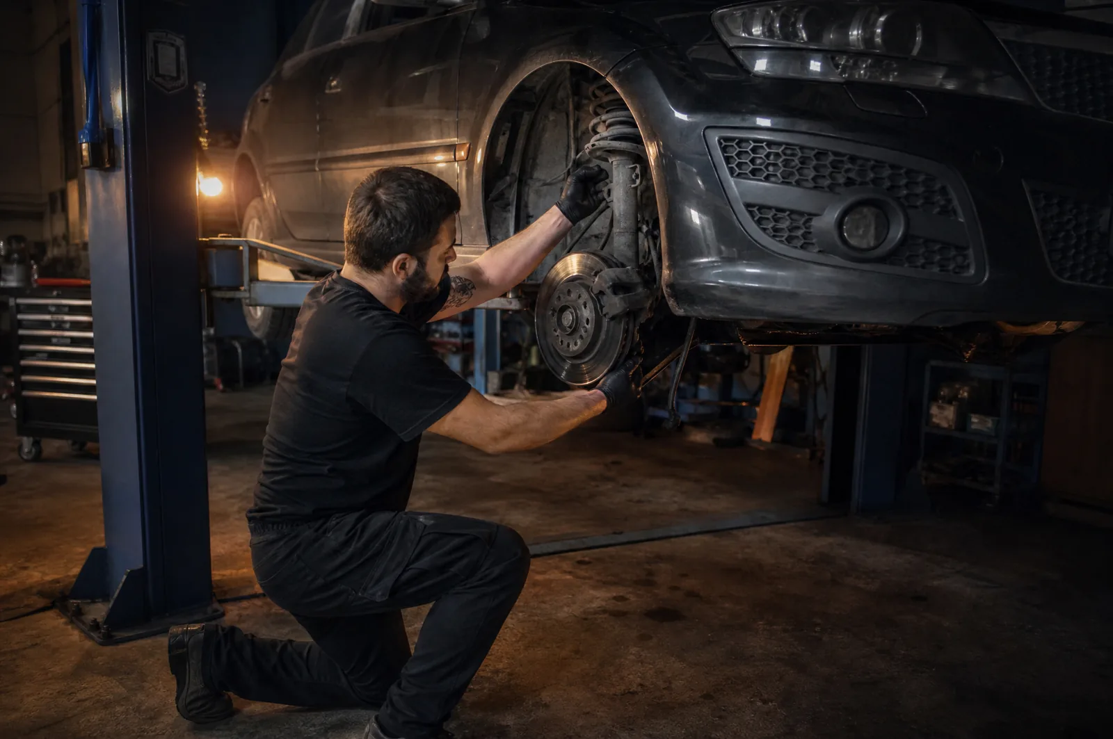 Mechaniker kniet am offenen Radkasten eines Autos auf der Hebebühne